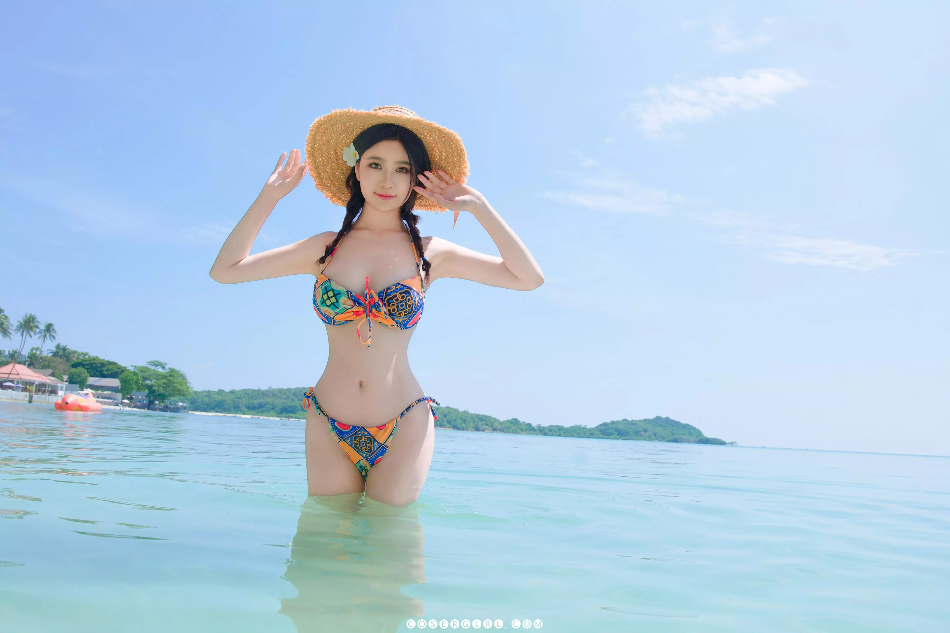 Coser年年双手扶着草帽,站在海水中正面看着镜头,笑容甜美。