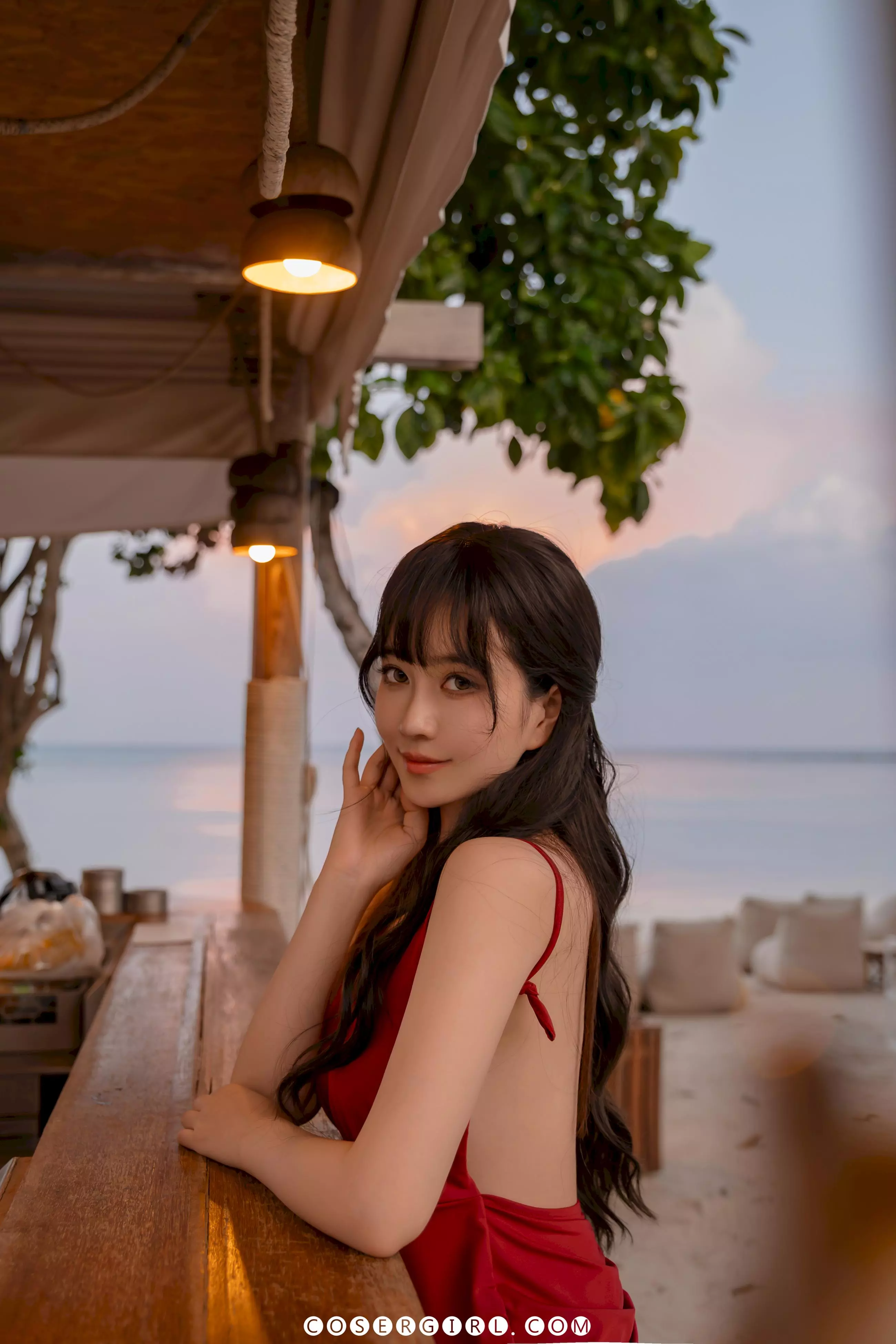 Coser年年坐在海边吧台,侧脸微笑,背景是黄昏海景