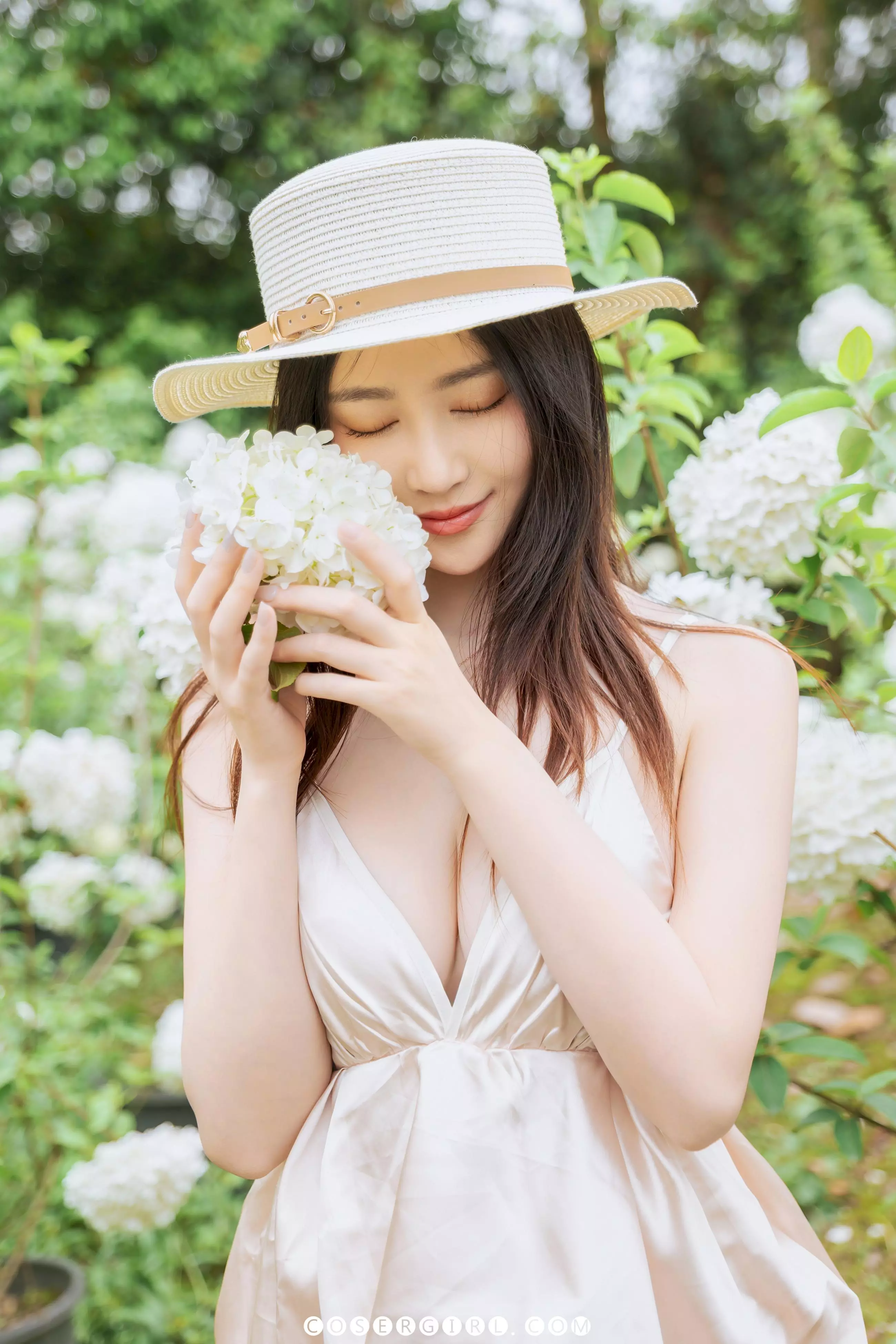 Coser年年站在白色木绣球花海中,手持一朵花轻触脸颊,回眸凝视