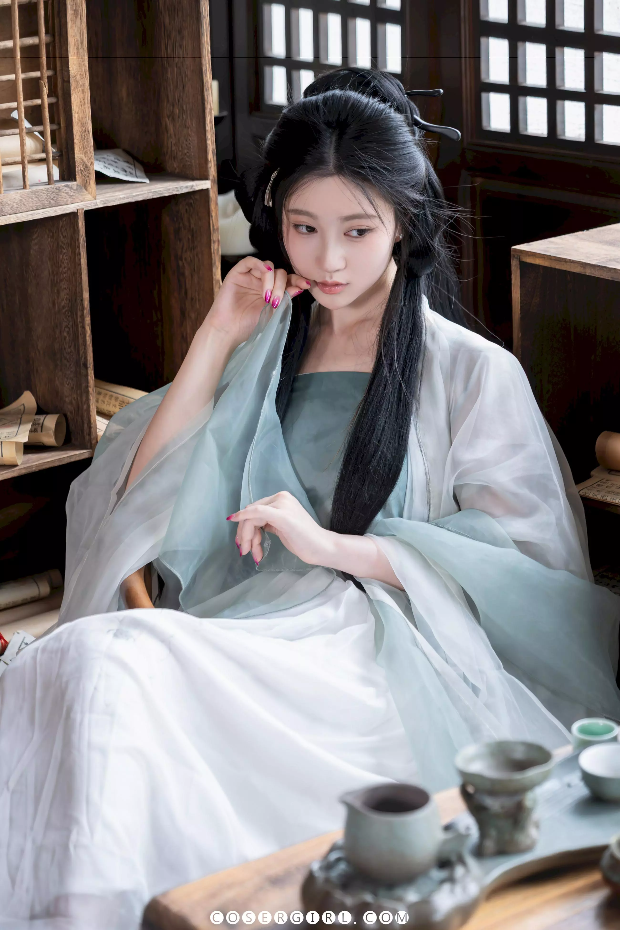 年年身着汉服坐在书桌旁,手指轻触下唇,眼神略带忧思