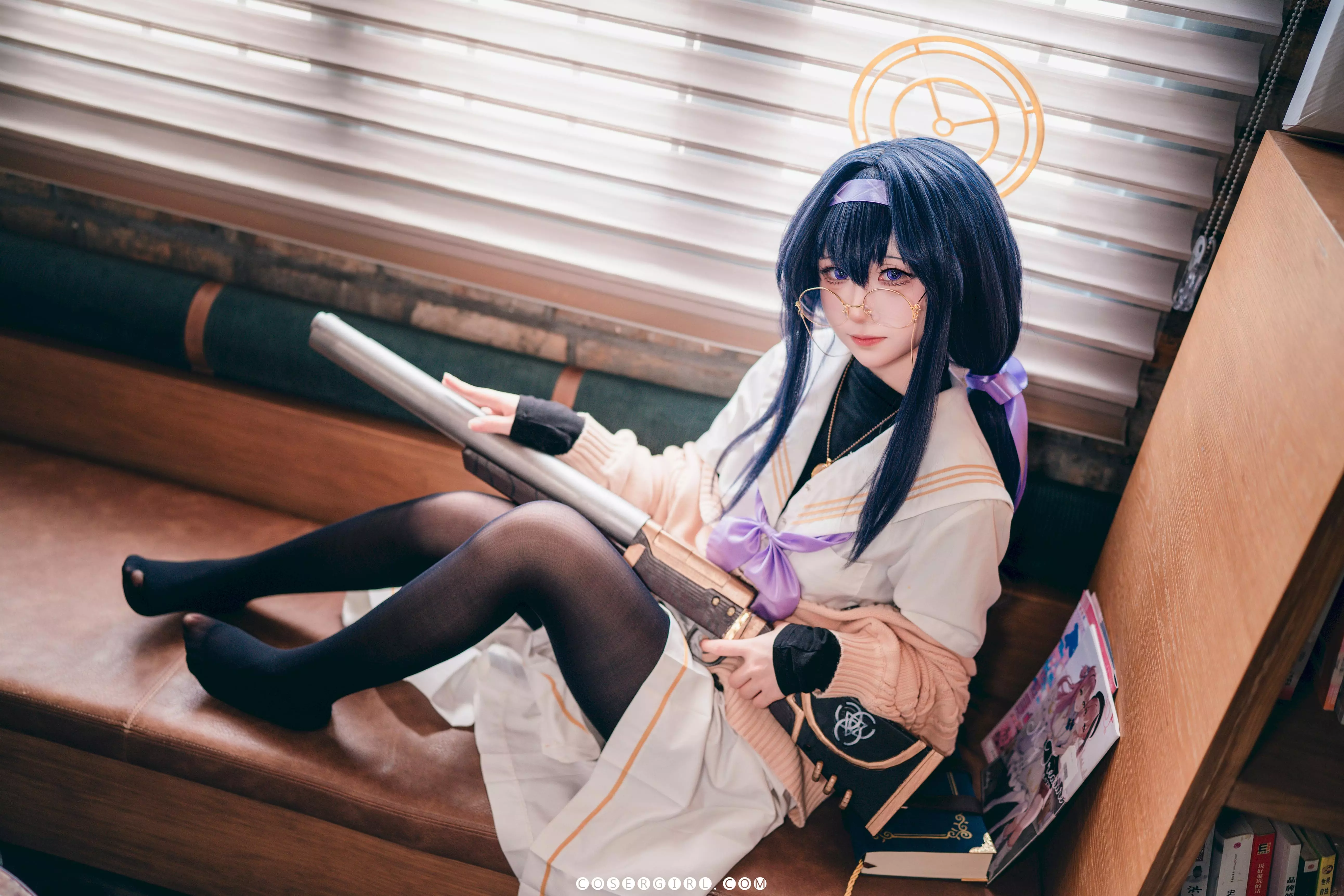 ran3扮演的古关忧坐在沙发上,侧身望着窗外,手里拿着一本深蓝色封面的书,姿态优雅。