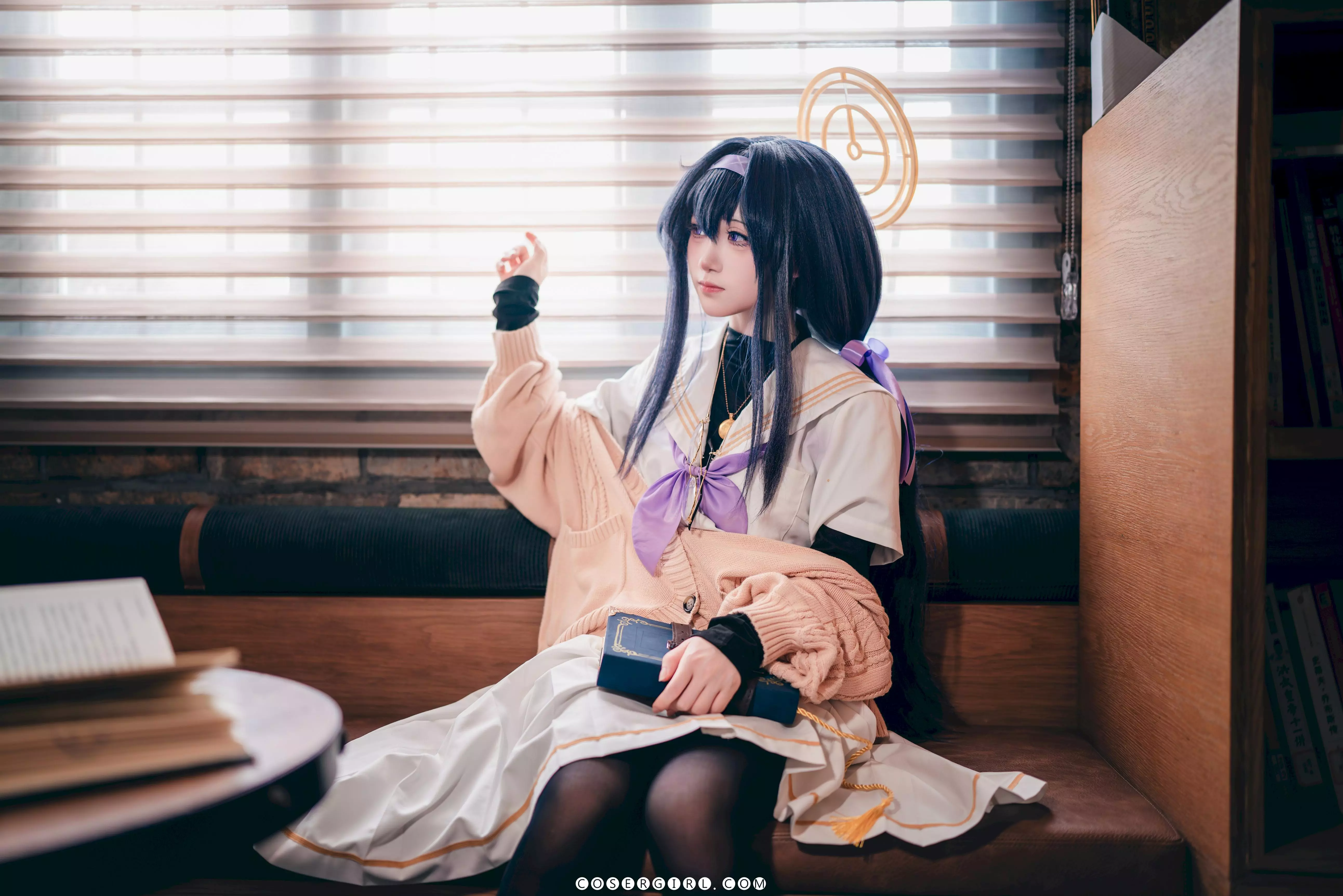 ran3扮演的古关忧坐在沙发角落,双手抱着一本黑皮书放在胸前,戴着眼镜,眼神略带羞涩地看向一旁。