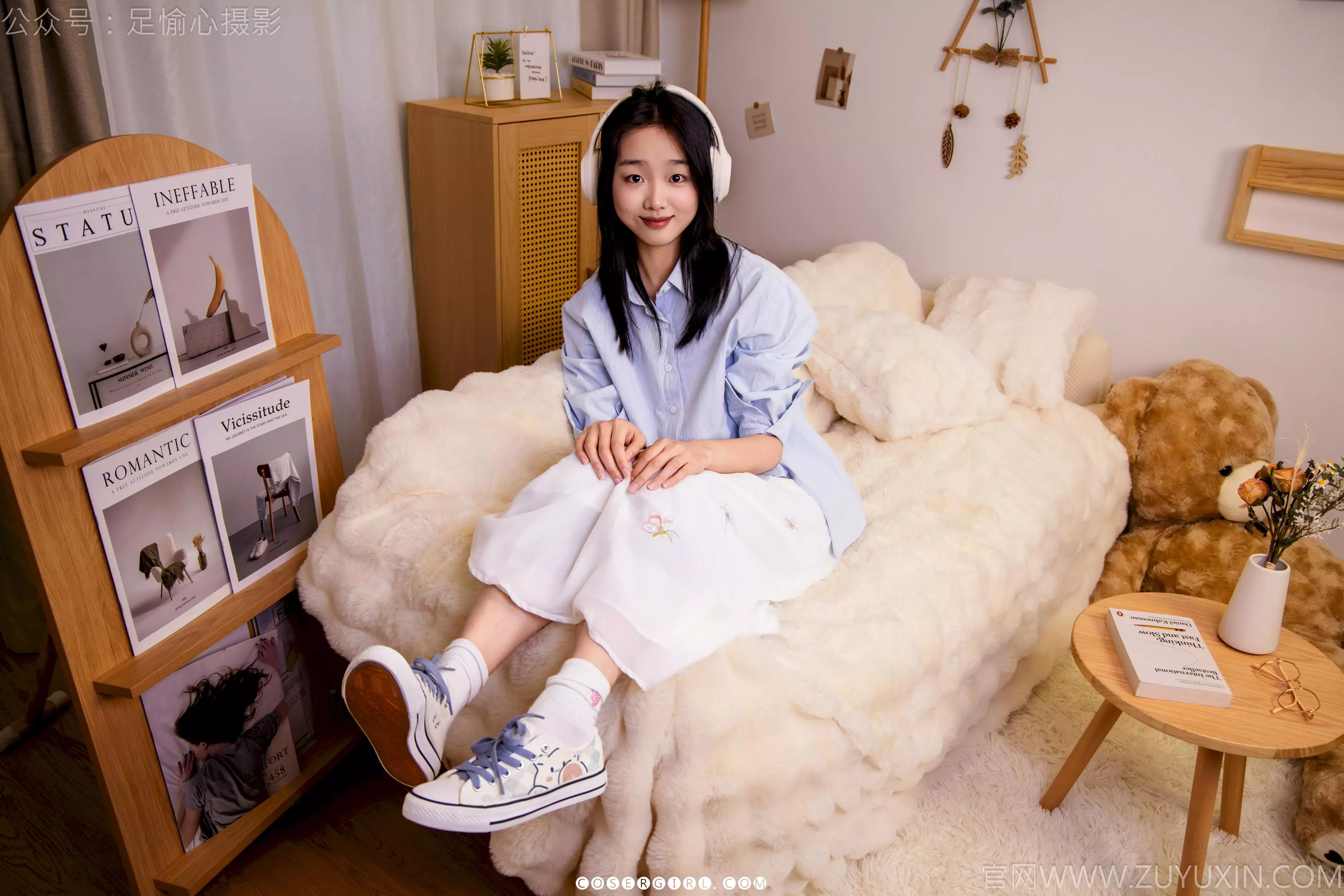 足愉心坐在毛绒床上，戴着耳机，身后是杂志架和泰迪熊，她微笑着看向镜头，姿态放松。