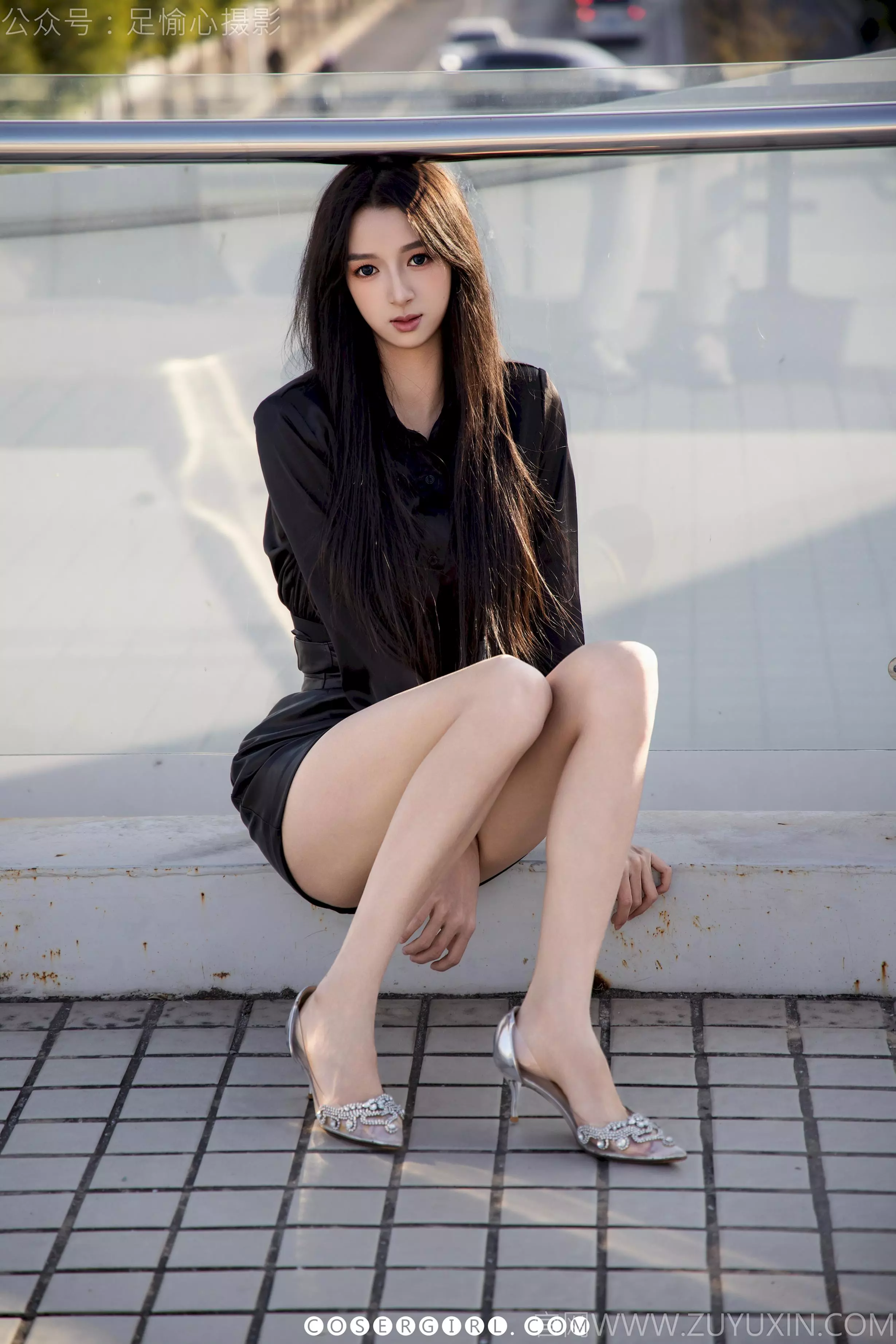 足愉心坐在绿色的草地上，黑色皮裙勾勒出曲线，她脱下了高跟鞋，赤足放松地摆放，眼神温柔地看着镜头。