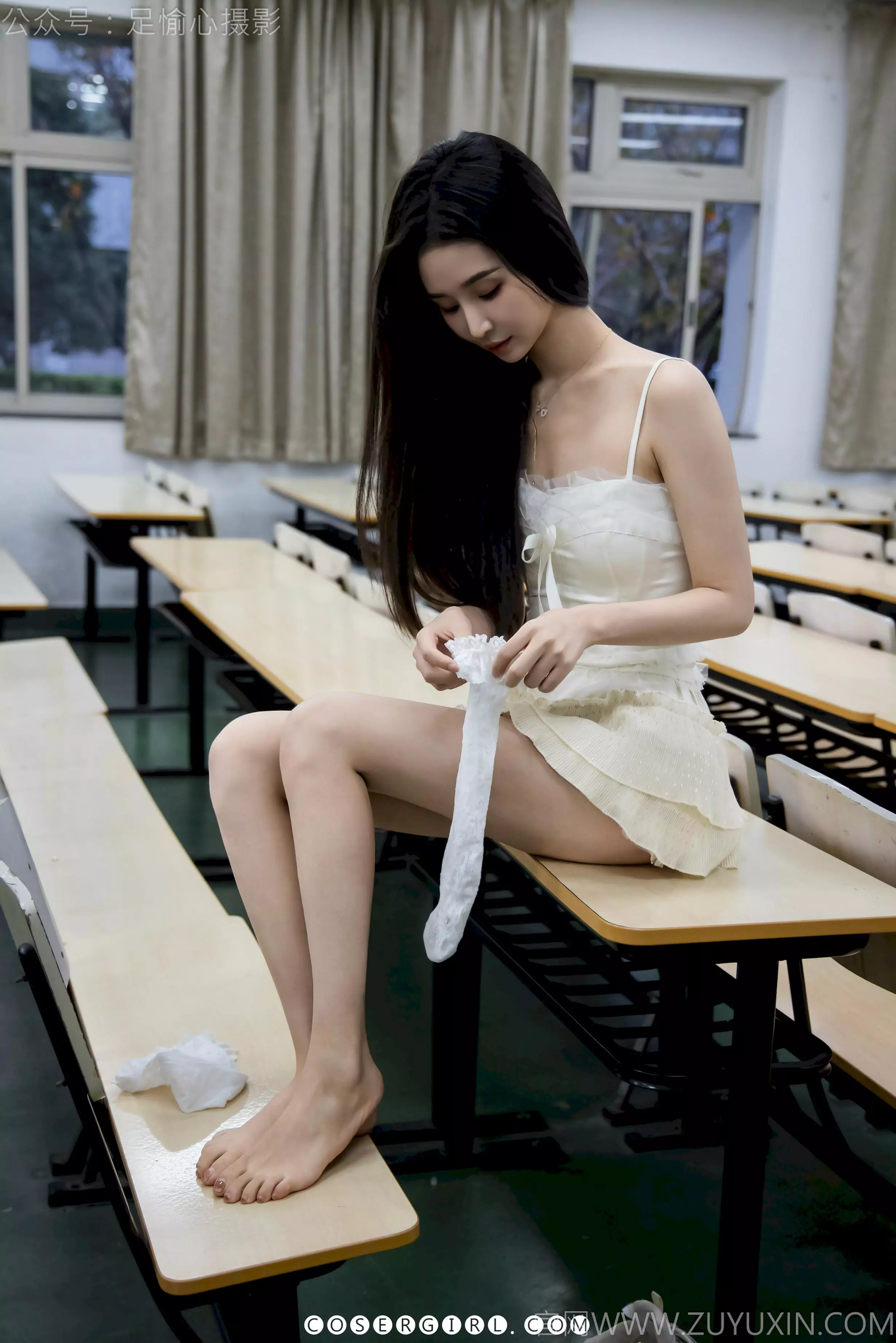 足愉心坐在课桌上，双腿交叠，正在将一只脱下的白色蕾丝长袜重新穿上，神情专注。